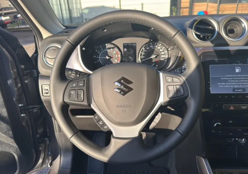 Vue intérieure centrée sur le volant noir du Suzuki Vitara 2025, avec tableau de bord et écran tactile allumé.