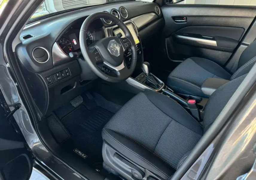 Intérieur côté conducteur du Suzuki Vitara 2025 gris argent, montrant tableau de bord, volant multifonction et sièges tissu noirs.