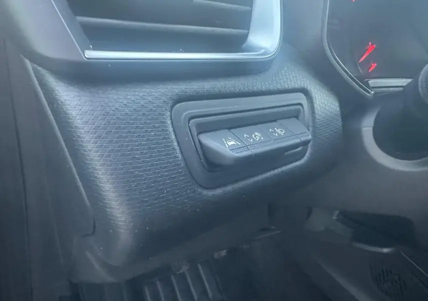 Gros plan sur les commandes d'aide à la conduite à gauche du volant dans l'habitacle sombre d'une Renault Clio gris foncé.