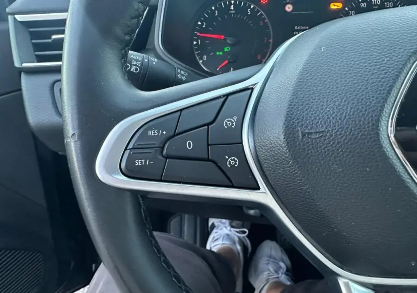 Gros plan sur le volant noir de la Renault Clio 2022, montrant les commandes du régulateur de vitesse côté gauche.