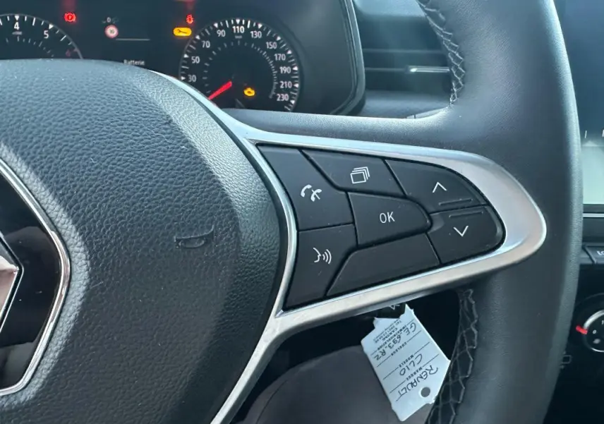 Gros plan sur le volant noir de la Renault Clio gris foncé 2022, avec commandes multifonctions et tableau de bord éclairé.