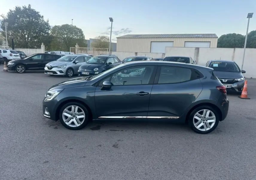 Profil côté gauche d'une Renault Clio gris foncé 2022 V TCe 90 Business, stationnée sur un parking extérieur.