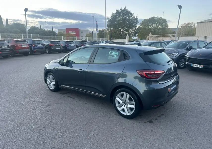 Renault Clio gris foncé vue 3/4 arrière droit sur parking, avec jantes alliage et vitres teintées.