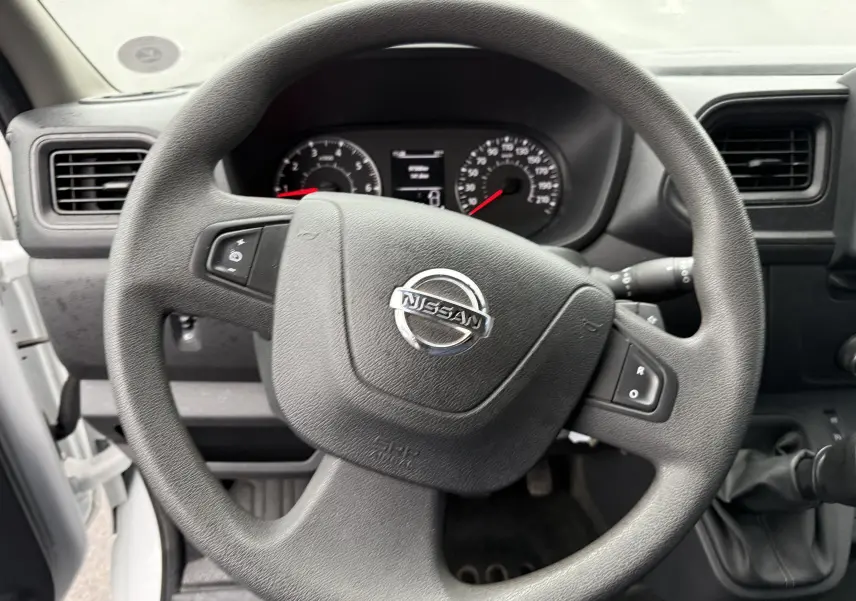 Vue rapprochée du volant noir du Nissan NV400 Fourgon 2020 avec tableau de bord et levier de vitesse manuel visibles.