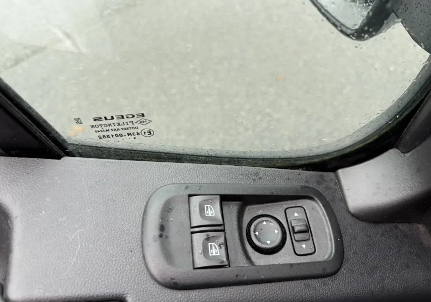 Gros plan sur les commandes électriques des vitres et rétroviseurs côté gauche du Nissan NV400 blanc, intérieur conducteur.