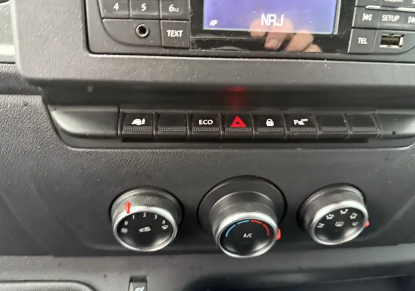 Gros plan sur la console centrale du Nissan NV400 blanc 2020, montrant les commandes de climatisation et les boutons de fonction.