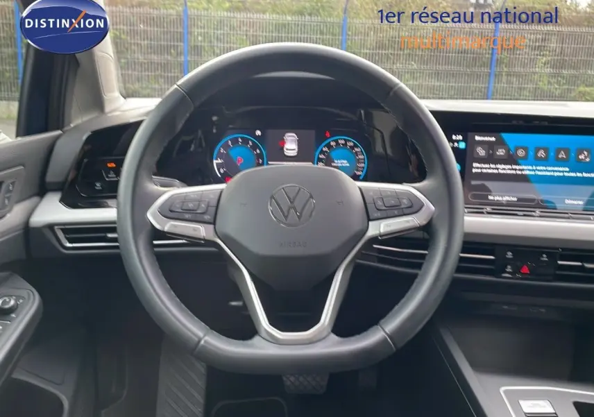 Volant cuir noir et tableau de bord digital d'une Volkswagen Golf VIII bleu lapiz metal, vue intérieure frontale.