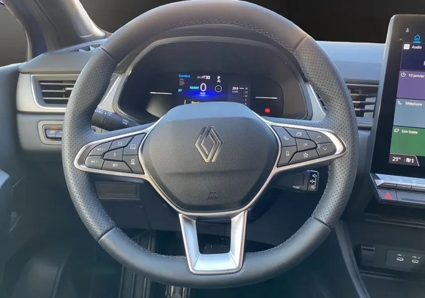 Vue rapprochée du volant noir perforé du Renault Captur 2025 avec tableau de bord numérique et écran tactile à droite.