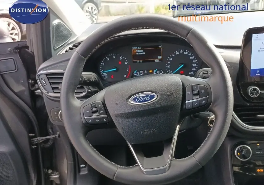 Vue intérieure centrée sur le volant Ford Puma gris foncé, tableau de bord et écran tactile visibles côté conducteur.