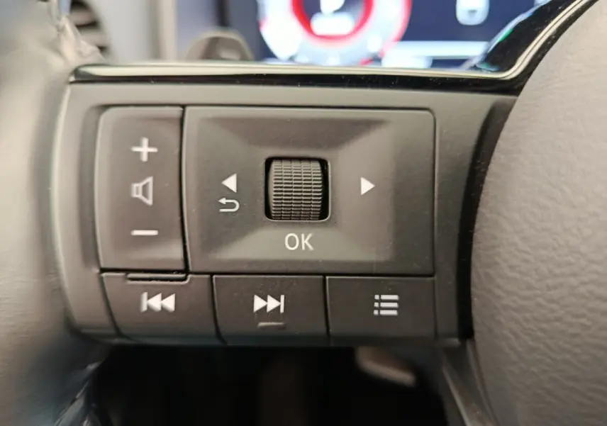 Gros plan sur les commandes multifonctions noires du volant du Nissan Qashqai 2023, avec boutons de réglage et navigation.