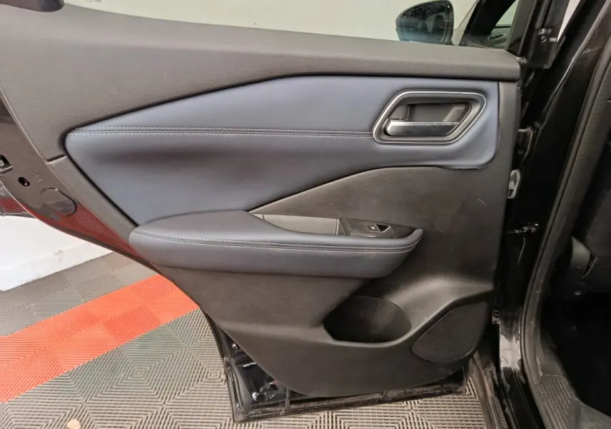 Vue intérieure de la porte arrière gauche noire du Nissan Qashqai 2023 avec accoudoir et commande de vitre.