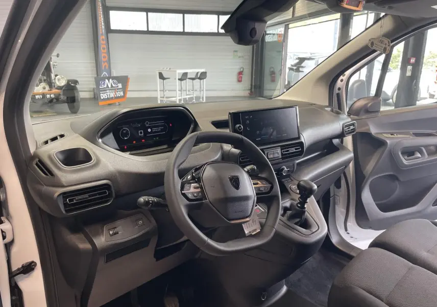 Vue intérieure côté conducteur du Peugeot Partner blanc 2026, montrant le tableau de bord et la console centrale avec boîte manuelle.