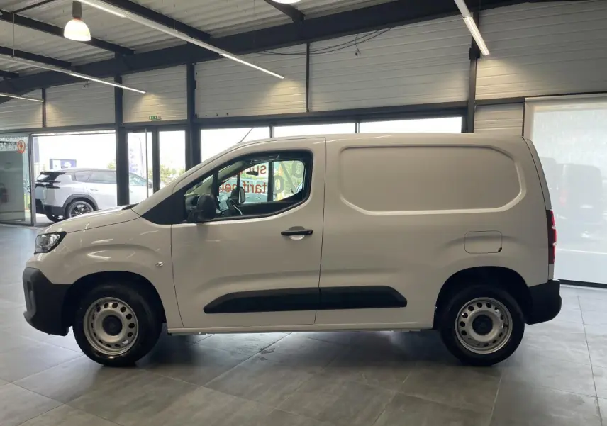 Peugeot Partner blanc en profil droit dans un showroom, avec jantes tôle grises et porte latérale coulissante.