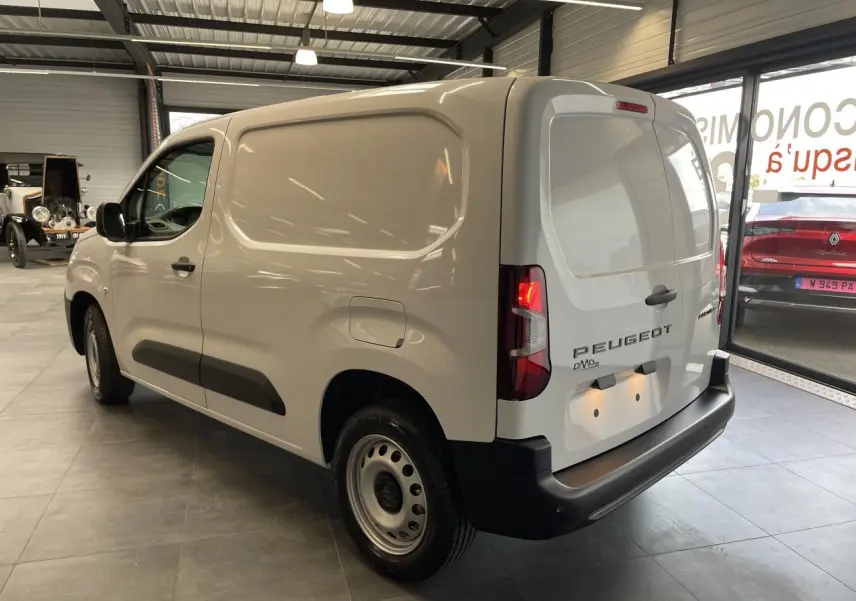 Vue 3/4 arrière droite du Peugeot Partner blanc, fourgon tôlé avec jantes tôle grises en showroom.