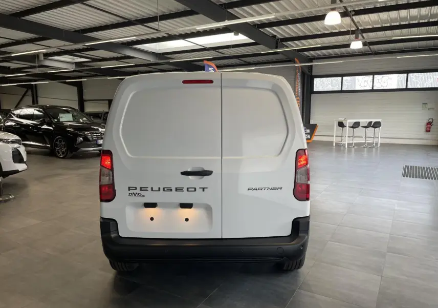Vue arrière d’un Peugeot Partner blanc stationné en intérieur avec portes battantes fermées et feux allumés.