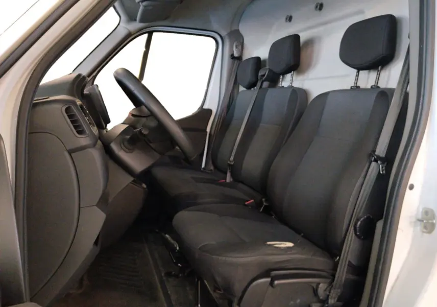 Vue intérieure côté conducteur du Renault Master blanc 2023, montrant les trois sièges noirs et le tableau de bord simple.