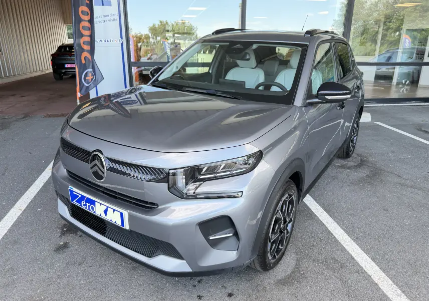 Citroën E-C3 113 MAX gris Mercury en 3/4 avant droit, avec jantes alliage 17 pouces et intérieur clair visible.