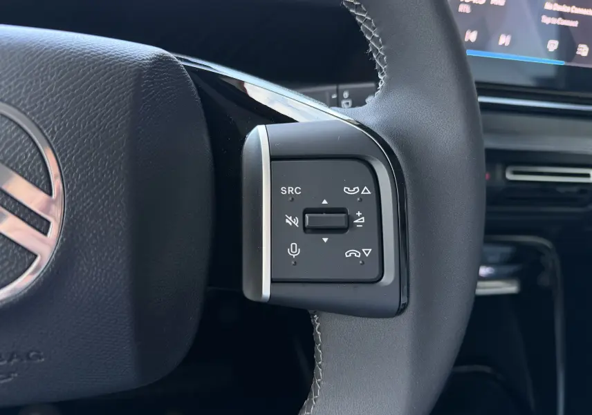 Gros plan sur les commandes multifonctions à droite du volant noir du Citroën E-C3 113 MAX 2025, avec écran tactile en arrière-plan.