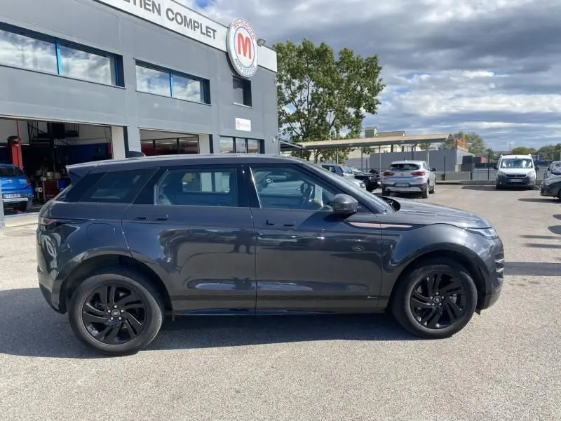 Vue de profil côté gauche d'un Range Rover Evoque gris foncé métallisé avec jantes noires, stationné devant un garage.