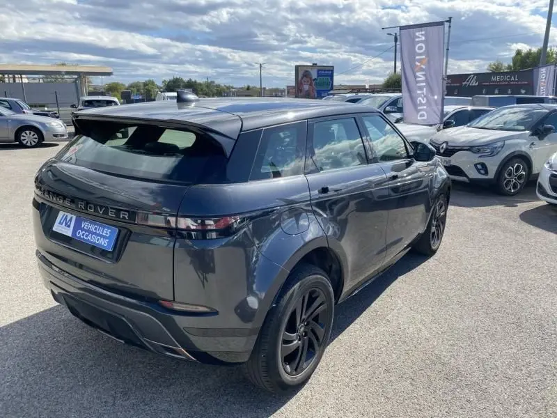 Vue 3/4 arrière droite d'un Range Rover Evoque gris foncé métallisé 2019 avec jantes noires sur parking extérieur.