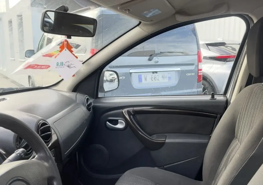 Vue intérieure côté conducteur du Dacia Duster 2011, montrant le volant, levier de vitesse manuel et siège tissu gris.