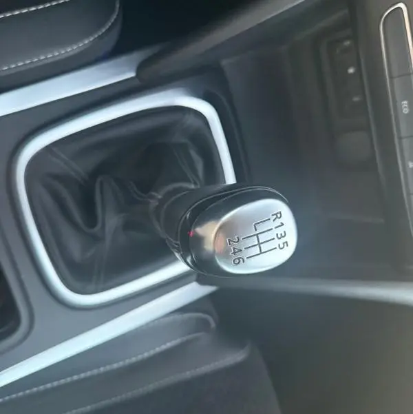 Gros plan sur le levier de vitesses manuel noir et argenté de la Renault Mégane IV gris clair, intérieur cuir noir.