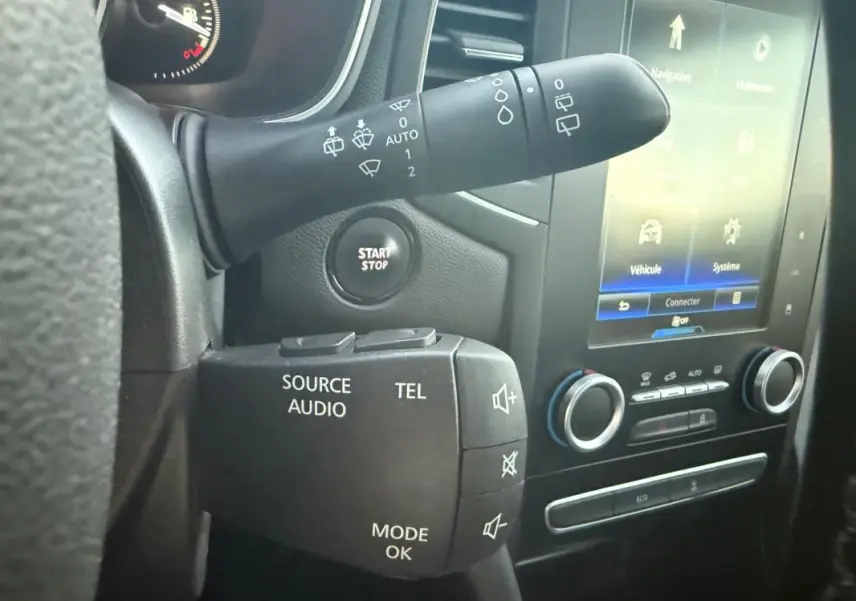 Détail intérieur montrant les commandes au volant et l'écran tactile de la Renault Mégane IV gris clair de 2016.