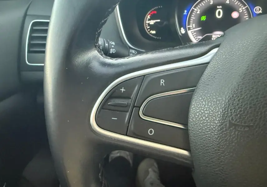 Gros plan sur le volant cuir de la Renault Mégane IV gris clair, avec commandes intégrées et tableau de bord en arrière-plan.