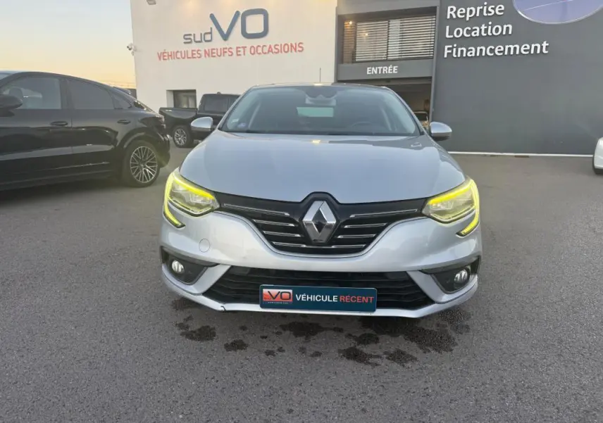 Vue frontale d'une Renault Mégane IV gris clair avec phares allumés et calandre noire brillante.