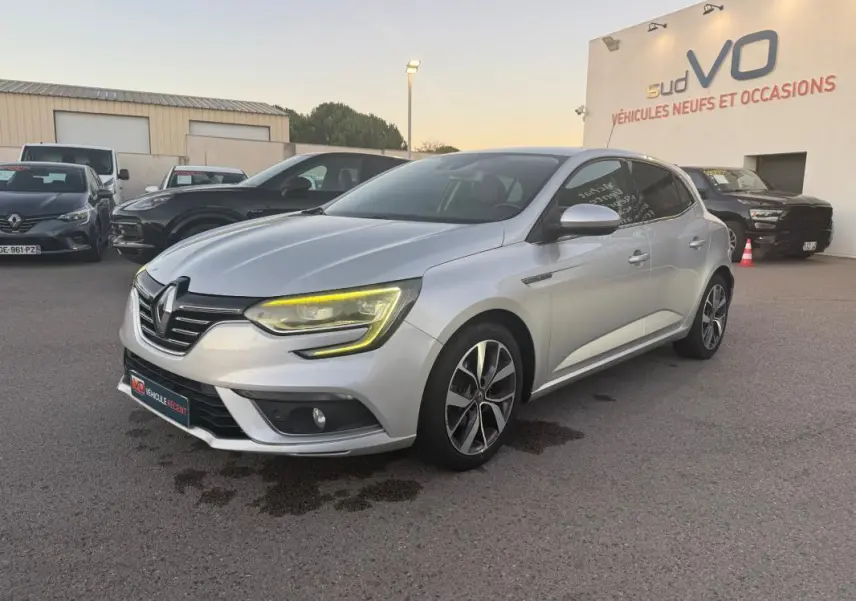 Renault Mégane IV gris clair vue 3/4 avant droit, jantes alliage 18 pouces et feux LED allumés.