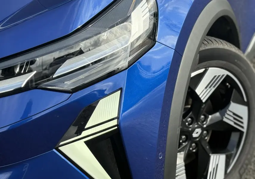 Gros plan sur l'avant droit bleu Iron du Renault SYMBIOZ 2025, mettant en valeur le phare LED et la jante 18 pouces.