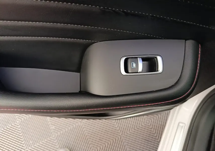 Détail de la commande de lève-vitre côté conducteur sur porte intérieure noire avec surpiqûres rouges d’un MG Motor EHS blanc.