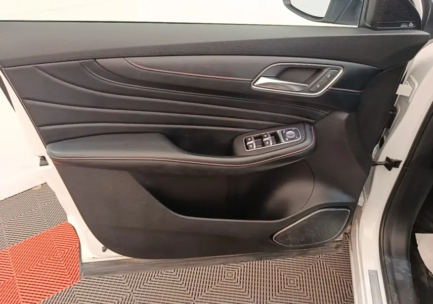 Porte avant gauche ouverte d’un MG Motor EHS blanc, intérieur noir avec surpiqûres rouges et commandes électriques.