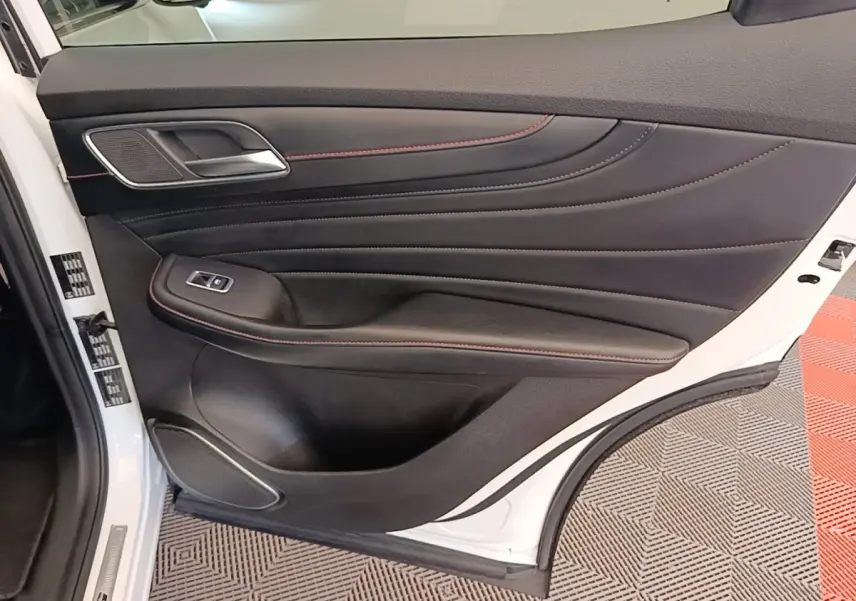 Intérieur de la porte arrière gauche du MG Motor EHS blanc, avec garniture noire et surpiqûres rouges visibles.