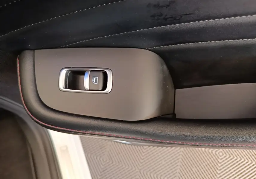 Détail de la commande de lève-vitre sur la porte intérieure noire avec surpiqûres rouges d’un MG MOTOR EHS blanc.