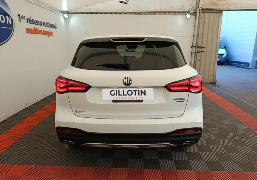 Vue arrière d’un MG Motor EHS blanc 2023 avec feux LED allumés dans un garage intérieur.