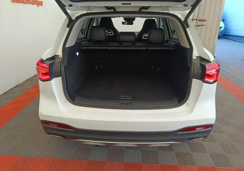 Vue arrière ouverte du coffre d’un MG MOTOR EHS blanc 2023, montrant l’espace de chargement et les feux arrière allumés.