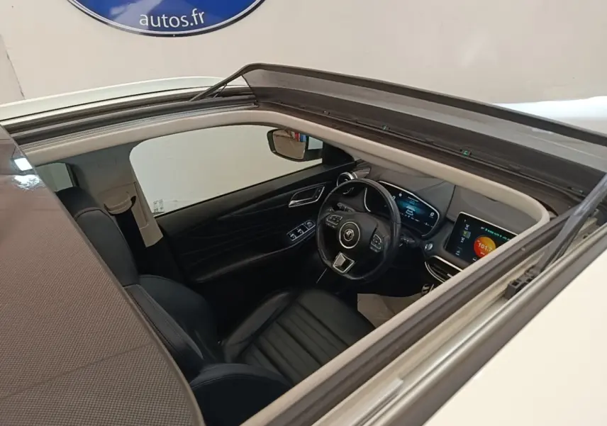 Vue intérieure par le toit ouvrant du poste de conduite du MG Motor EHS blanc avec tableau de bord digital et volant cuir.