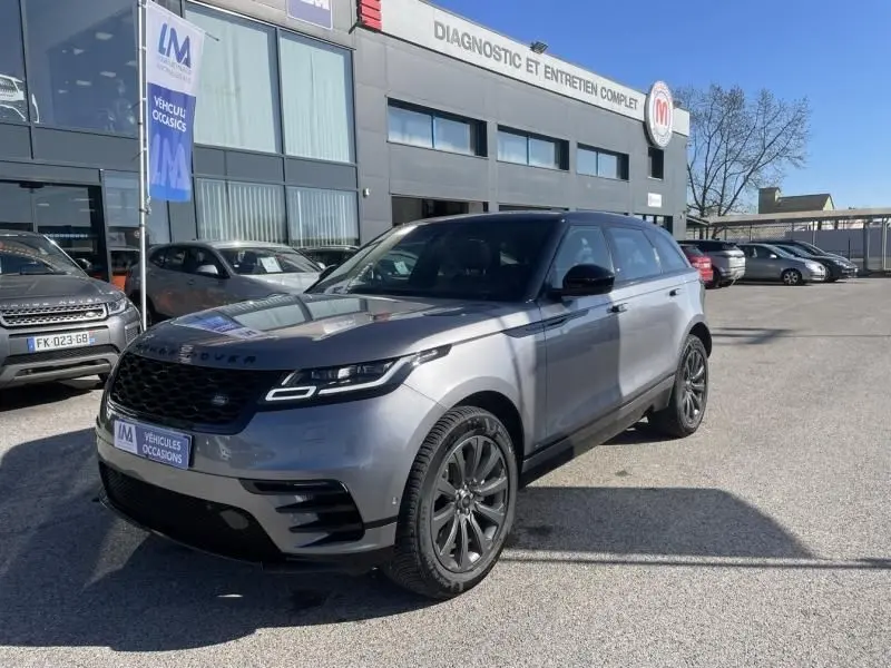 Vue 3/4 avant droit d'un Range Rover Velar gris métal 2020 garé devant un garage avec calandre noire distinctive.