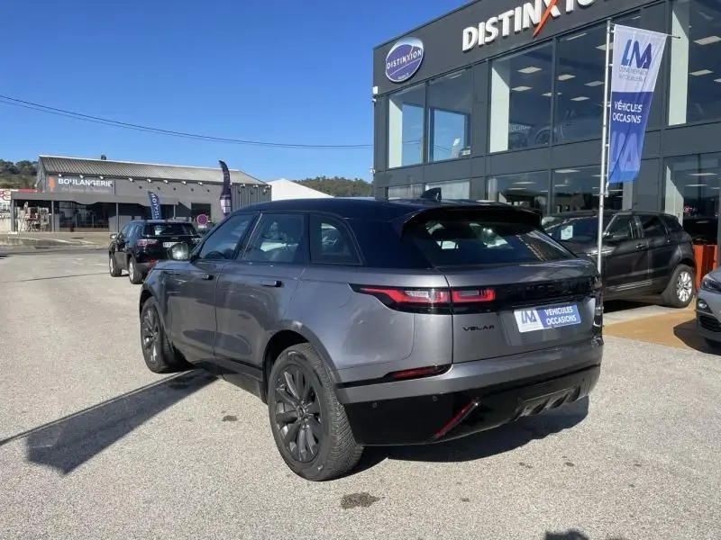 Vue 3/4 arrière droite d'un Range Rover Velar gris métal 2020 avec toit noir, garé devant un concessionnaire.