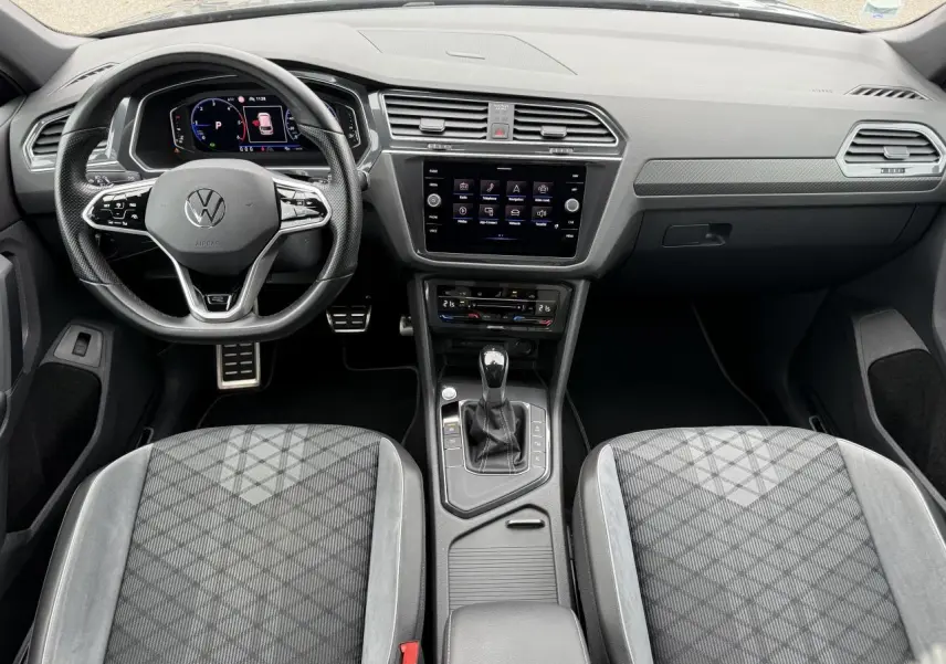 Vue intérieure frontale du Volkswagen Tiguan 2023, volant cuir multifonction et sièges sport en tissu gris.