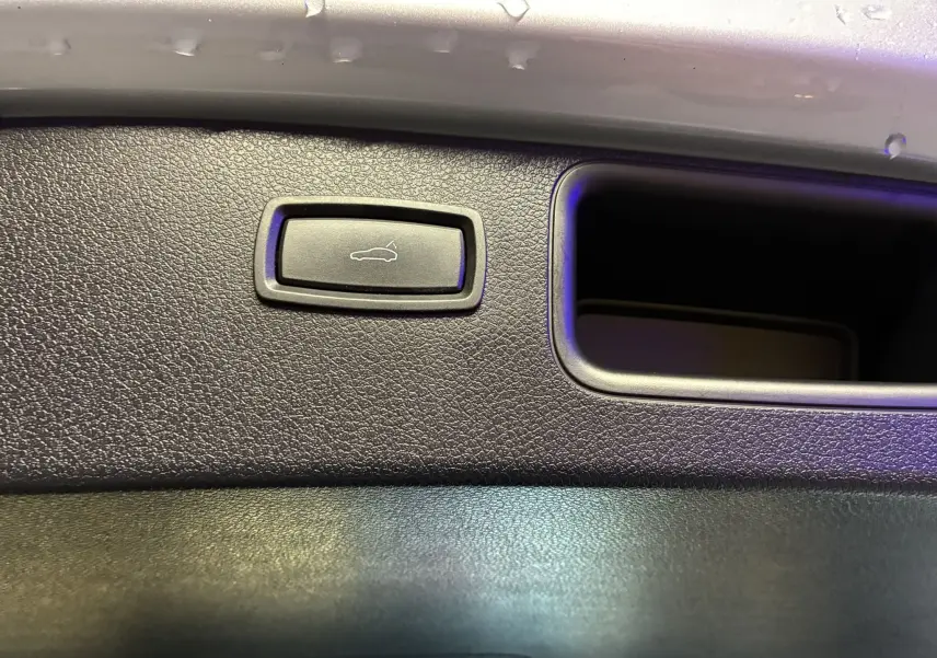 Gros plan sur le bouton d'ouverture du hayon intégré dans le panneau intérieur noir du coffre du Porsche Macan GTS 2017.