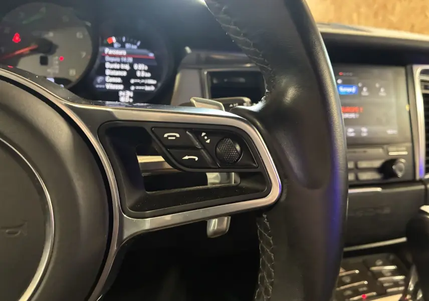 Gros plan sur le volant en cuir noir du Porsche Macan GTS 2017, avec commandes intégrées et tableau de bord numérique en arrière-plan.