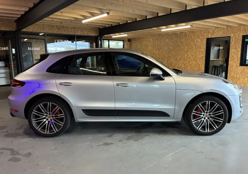 Profil droit d'un Porsche Macan 3.0 360 GTS essence gris clair avec jantes RS Spyder 20'' et étriers rouges, en intérieur.