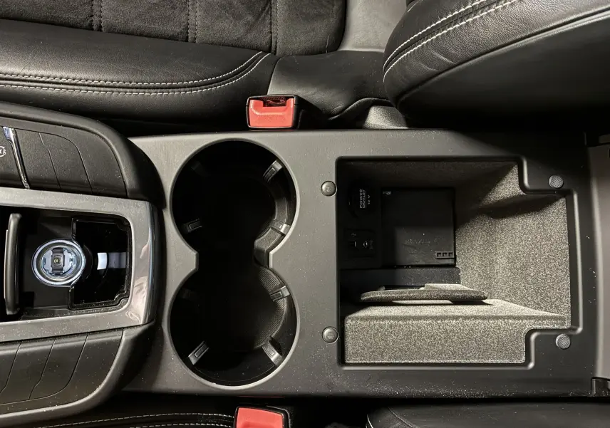 Vue plongeante sur la console centrale noire du Porsche Macan GTS 2017 avec porte-gobelets et compartiment ouvert.