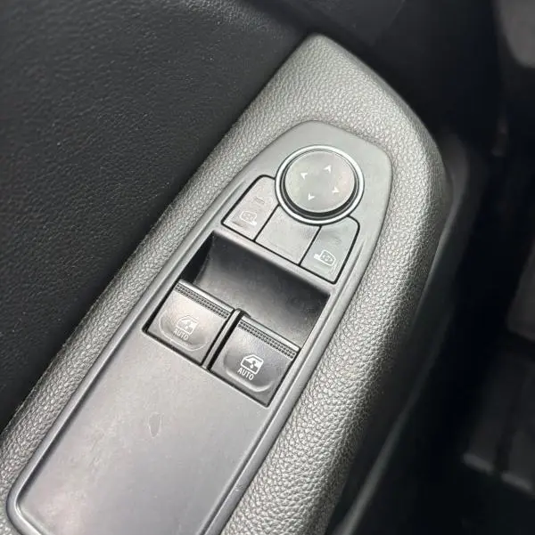 Gros plan sur les commandes de lève-vitres et réglage des rétroviseurs côté conducteur d'une Renault Clio gris foncé 2022.