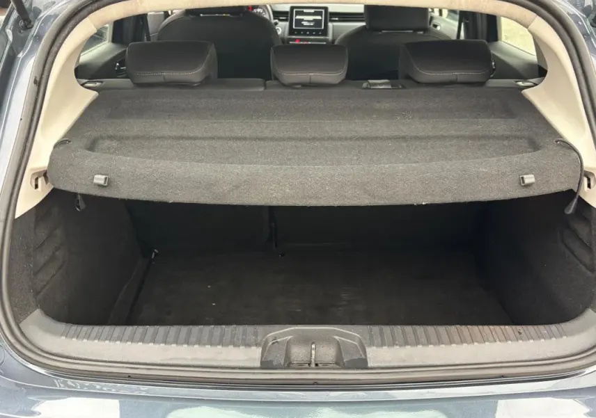 Coffre ouvert vu de l'arrière d'une Renault Clio gris foncé, montrant la plage arrière et les sièges arrière rabattus.