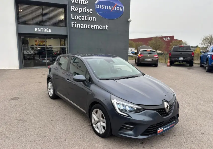 Renault Clio V TCe 90 gris foncé vue 3/4 avant droit, stationnée devant un garage avec enseigne Distinxion.