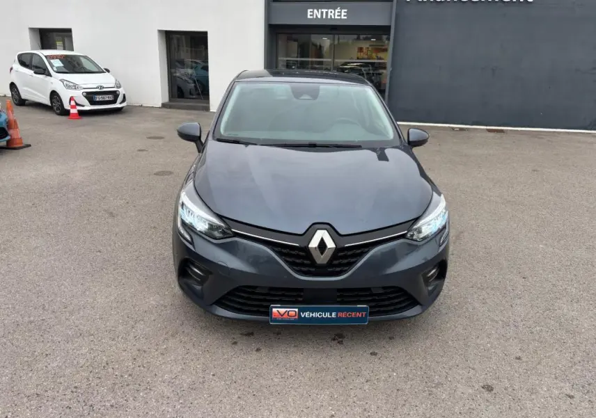 Vue frontale d'une Renault Clio V TCe 90 Equilibre gris foncé avec phares allumés sur un parking extérieur.