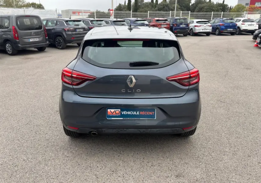 Vue arrière d'une Renault Clio gris foncé 2022, avec feux arrière allumés sur un parking extérieur.
